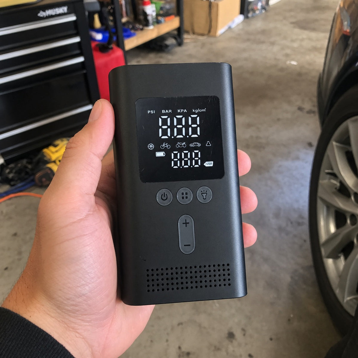 Crankbox jump starter and tire inflator held in a garage next to a car